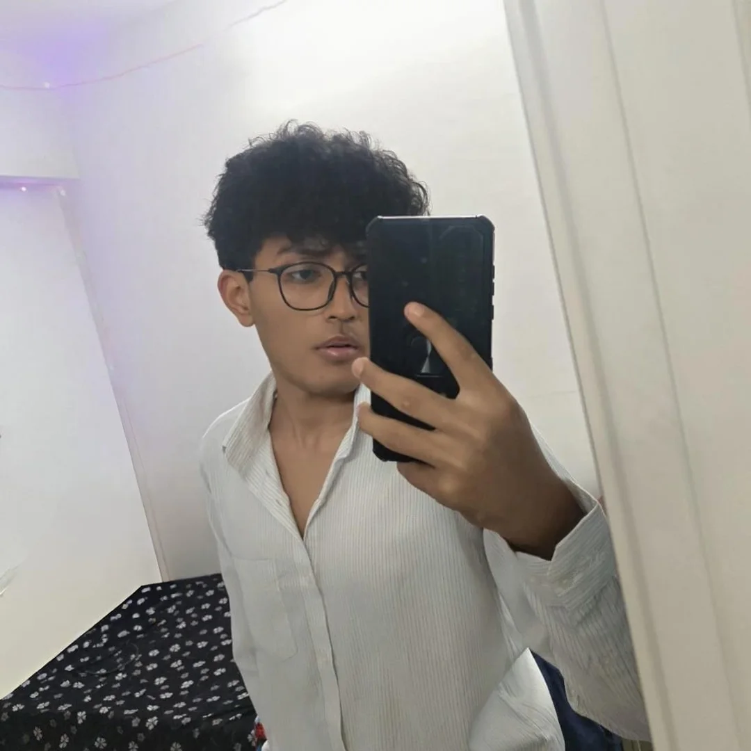 Aarush wearing glasses and a white shirt in a mirror photograph.