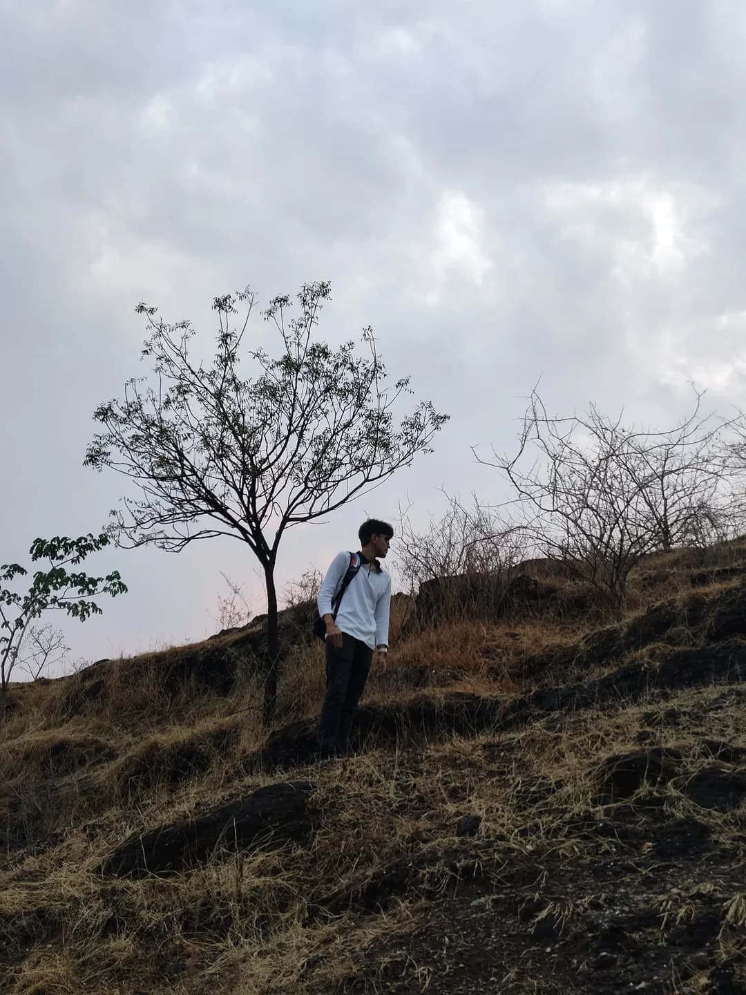 Aarush trekking across a rocky hillside beneath an overcast sky.