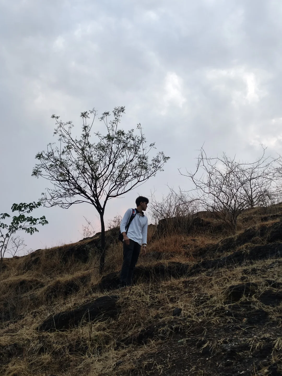 Aarush trekking across a rocky hillside beneath an overcast sky.